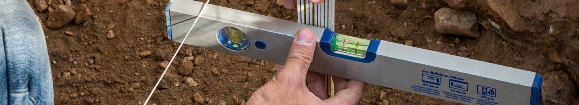 Hands hold a spirit level and ruler whilst recording an archaeological feature.