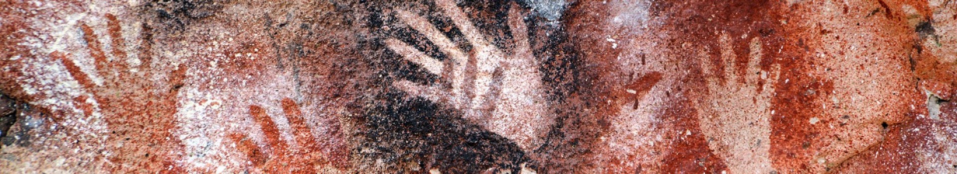 Ancient stencilled hand prints surrounded by black and orange dye on a cave wall.